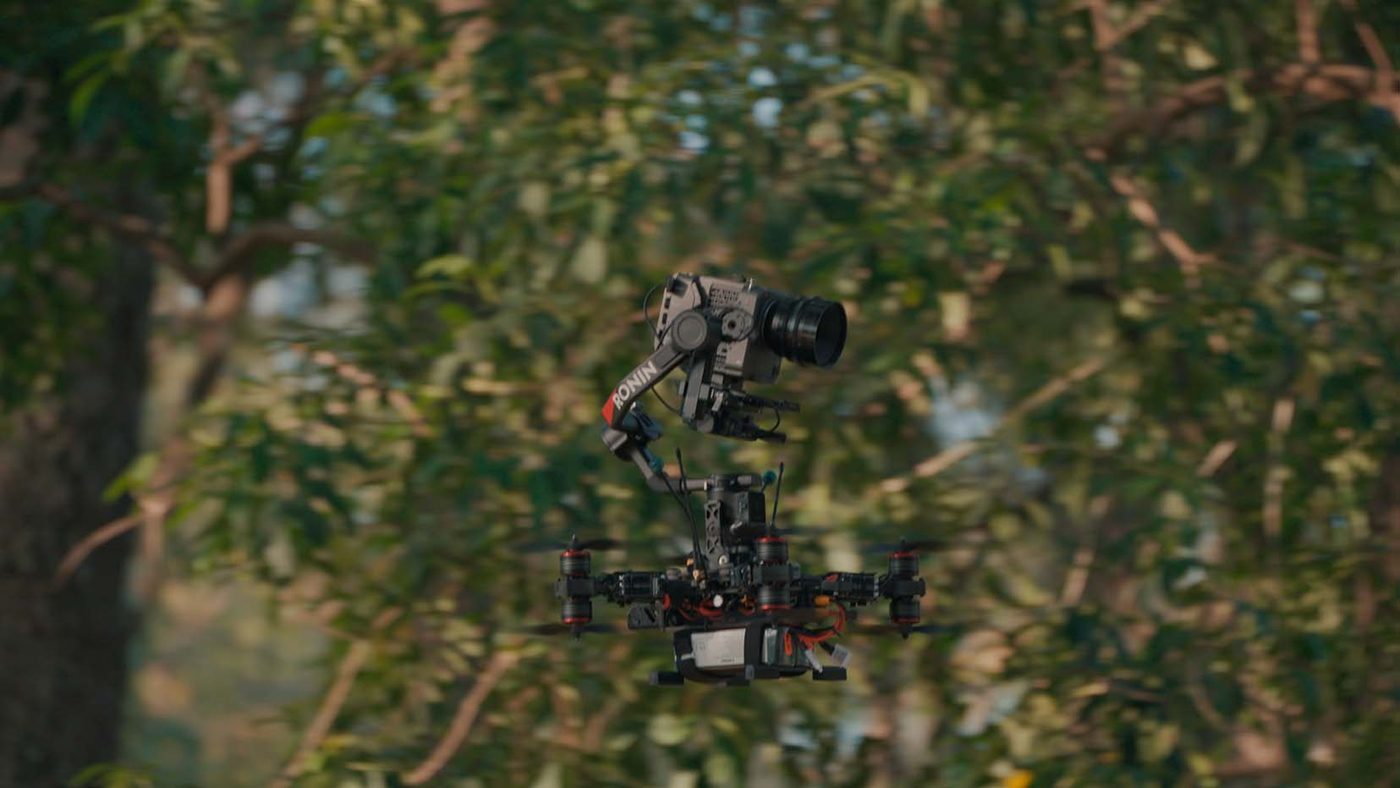 Drone de AIRA con cámara de cine y lente largo, volando entre el follaje de los árboles